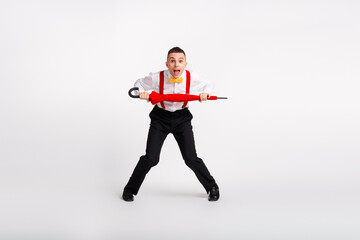 Young man in a playful dance pose holding a red umbrella, dressed in retro style with suspenders...