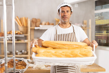 Bakery advertising banner. Caucasian male employee works in bakery kitchen, he demonstrate finished products baguettes, ready to provide bakerys customers with fresh products and goods