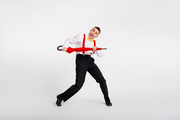 Young man in vibrant retro style dancing playfully with a red umbrella against a white background