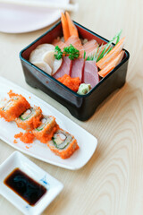 Sashimi and sushi rolls served with soy sauce on wooden table