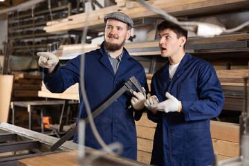 Two young male carpenters discussing work process in wood workshop