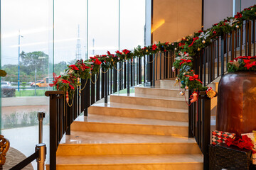 Embrace the festive spirit with this elegant image of a staircase adorned with Christmas garlands. The warm lighting, lush greenery, and vibrant red accents create a welcoming atmosphere.
