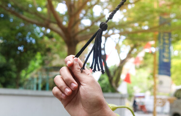 Hands holding graduation cap string to celebrate graduation day, focus on graduation cap string with garden background