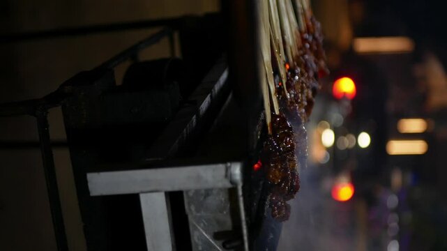 Chicken sate or satay on fiery charcoal grilling by people in Indonesia with blurred street, car, motorcycle background, vertical video