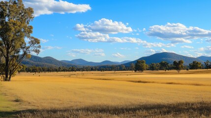 Obraz premium A serene landscape featuring golden fields, distant mountains, and a clear blue sky.