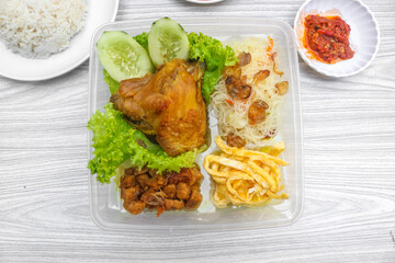 Yellow rice with side dishes of chicken, tempeh, scrambled eggs, noodles and chili sauce is served on a plate. Indonesian style yellow rice