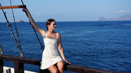 Young beautiful slim woman in white dress traveling on yacht. Beautiful woman posing for photo on yacht during vacation in Indonesia