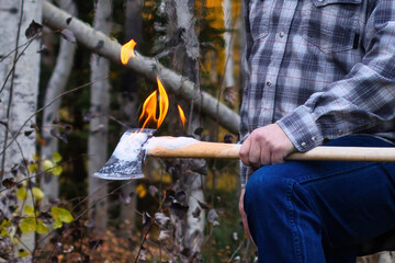 Flames coming off an axe a man is holding over his knee on an autumn day in Alaska.