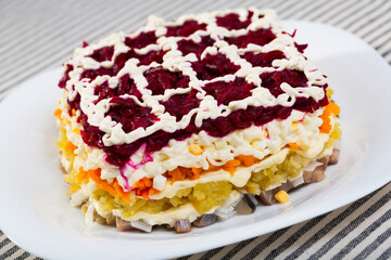 Delicious Russian Dressed herring salad served on white plate on striped textile background..