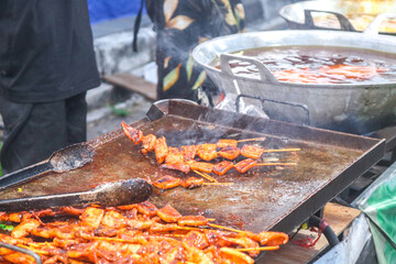 Close up of a chef's hands grilling sausage, grilled squid, on a BBQ, on the hot grill with torch fire. BBQ street food