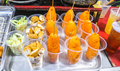 Freshly fried corn dogs and tofu in cup displayed at a night food festival. Street food corn dogs stuffed with cheese are sold at a food stand