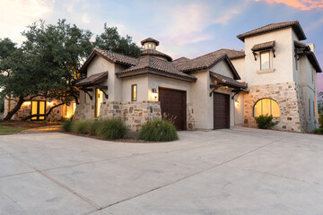 Elegant modern home with stone accents and a spacious driveway at sunset