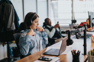 Fototapeta premium A young business employee focused on her computer while wearing headphones in a contemporary office setting. Technology and modernity blend in a productive workspace.
