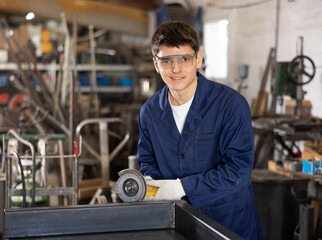 Portrait of young mechanic in safety glasses with an angle grinder in his hands. Work at a machine-building plant