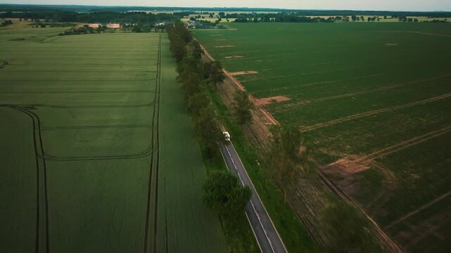 Aerial view following a RV driving in a alley, in middle of countryside fields