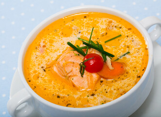 Picture of delicious soup with salmon, served in white bowl at table