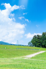Obraz premium Winding path through a green grass field in hilly area against blue sky with clouds,Pathway s curve in public park.