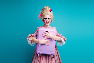 Portrait of young astonished princess girl hold suitcase wear vintage dress isolated on turquoise color background