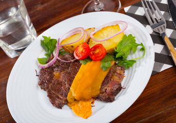 Well-done beef steak with baked potatoes and cheese served at plate with greens