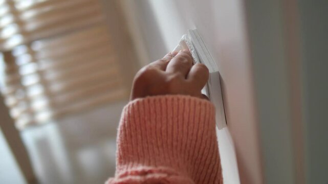hand with tissue wiping a light switch at the wall