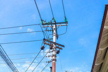 High voltage electric pole with many cables in residential area with blue sky background. The...