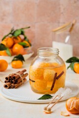 Whole tangerines in syrup with cinnamon sticks and vanilla in a glass jar on a light concrete background. Sweets, preserves, preparations.