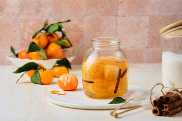 Whole tangerines in syrup with cinnamon sticks and vanilla in a glass jar on a light concrete background. Sweets, preserves, preparations.