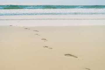 Footprints of human feet on the sand near the water on the beach.