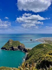 Stunning scenery along New Zealand coastal hike. Photo overlooks greenish-blue water, black sand beaches and green surroundings. 