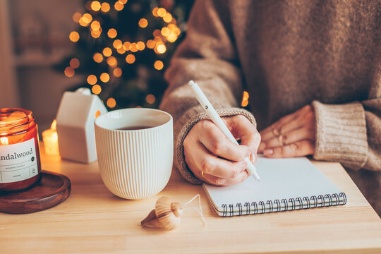 Cozy winter still life. Women writing goals and plans in notebook, drinking a mug with tea or coffee, burning candle. Seasonal holidays and hygge concept