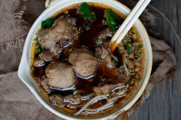 A traditional Thai beef noodle soup, served in a ceramic bowl. The rich, aromatic broth is filled with tender beef, flavorful meatballs, and a variety of vegetables.