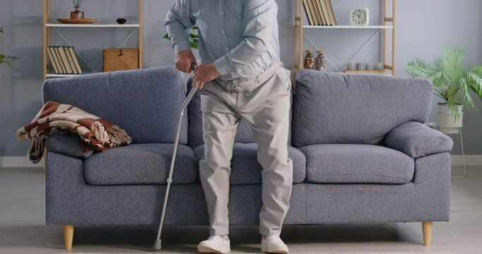 Retired old senior man, elderly person alone at home, sitting on couch, stands up using walking stick. Grandfather abandoned at nursing home, left one in room, feeling difficult to move, going away 