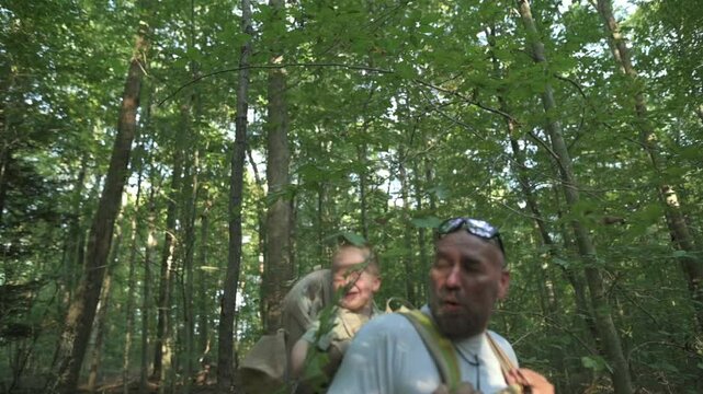 ather and baby enjoy scenic forest hike, surrounded by lush green foliage baby smiles while riding in comfortable backpack carrier under canopy of sunlight-filtered trees Father hiking with baby 