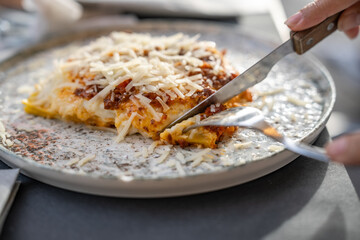 Close up freshly baked lasagna dish hand cutting.