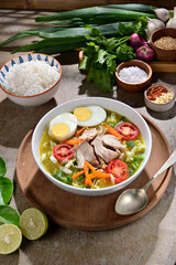 Soto Ayam Jogja is a Javanese chicken soup with clear broth, shredded chicken, vermicelli, hard-boiled egg, and spices, served with rice, lime, tomato slices and sambal.