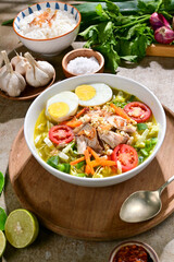 Soto Ayam Jogja is a Javanese chicken soup with clear broth, shredded chicken, vermicelli, hard-boiled egg, and spices, served with rice, lime, tomato slices and sambal.
