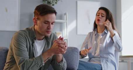 Angry wife shouting in quarrel on her unhappy upset husband sitting on sofa at home. Young couple quarreling and arguing in living room. Marriage problems, relationship and divorce concept. 4k video. - Powered by Adobe