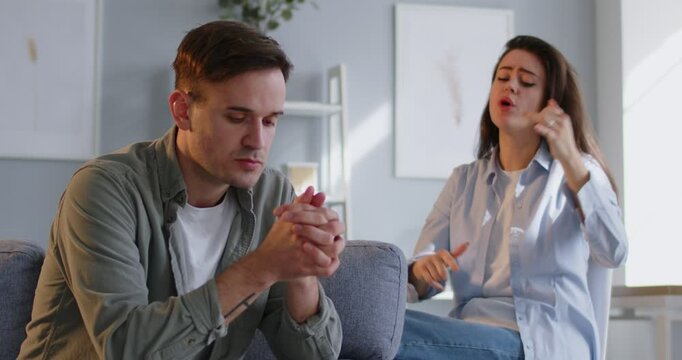 Angry wife shouting in quarrel on her unhappy upset husband sitting on sofa at home. Young couple quarreling and arguing in living room. Marriage problems, relationship and divorce concept. 4k video.