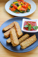 Pan fried Tempeh with homemade marinara sauce with blurry green salad in the backdrop