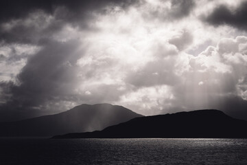 Fototapeta premium Stormy clouds over mountains with light rays hitting terrain and sea
