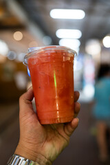 Watermelon smoothie in take away cup on man hand at night market