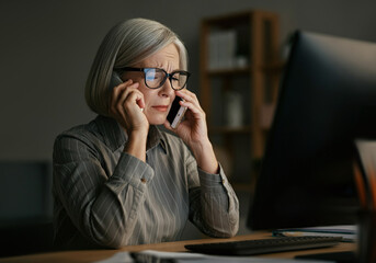 A mature woman in her 50s experiencing phone and vision problems, dealing with eyesight issues such as myopia or glaucoma in an office setting. Struggling to read blurry emails online while squinting,