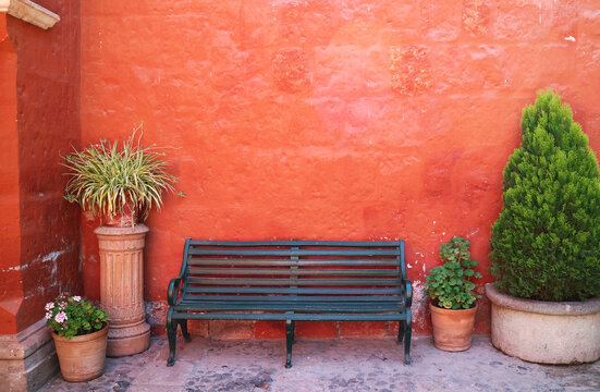 Black wooden bench outside orange red rough wall with potted plant in Santa Catalina monastery, Arequipa, Peru, South America