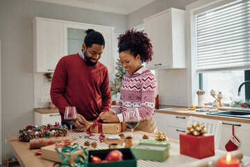 Happy black couple wrapping Christmas presents at home.