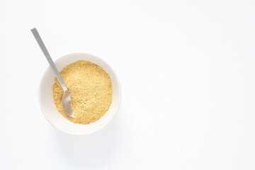 Top down view of a white bowl with nutritional yeast flakes and metal spoon on white background with copy space
