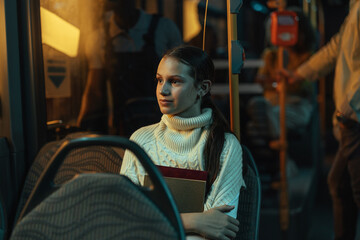 Female student holding books is sitting on a bus