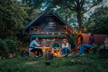 Friends hanging out by a campfire in the backyard of a forest cabin