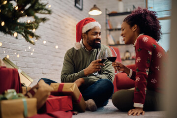 Fototapeta premium Smiling black couple toasting with wine while celebrating Christmas at home.