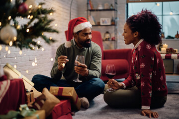 Fototapeta premium Smiling black couple talking while drinking wine on Christmas Eve at home.