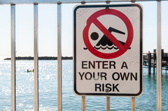 "No swimming" sign by railing overlooking a sunny waterfront